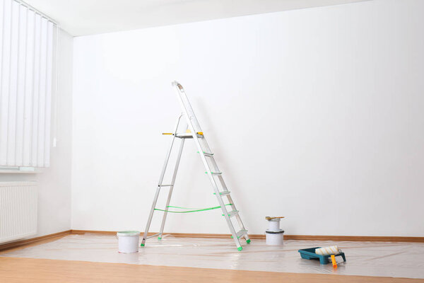 Лестница и инструменты для покраски у стены в пустой комнате