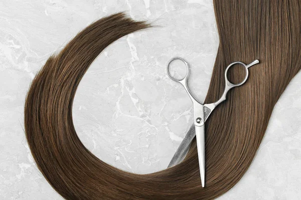 Плоска композиція з коричневим волоссям і ножицями на сірому фоні. Перукарське обслуговування — стокове фото