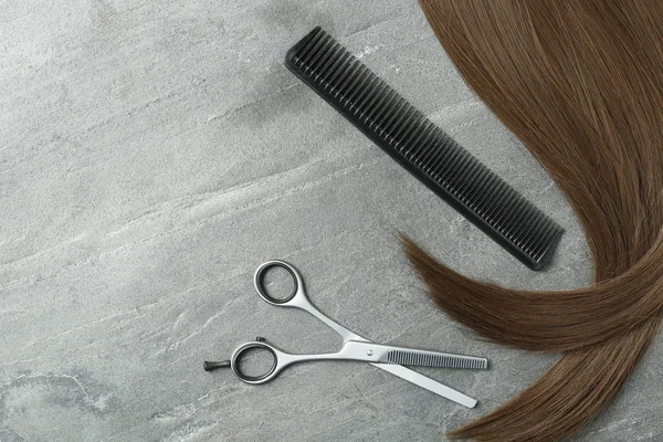 Flat lay composition with brown hair, comb, thinning scissors and space for text on grey background. Hairdresser service