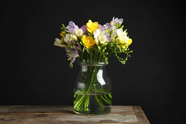 Ramo de flores frescas de freesia en jarrón de vidrio sobre la mesa sobre fondo negro — Foto de Stock