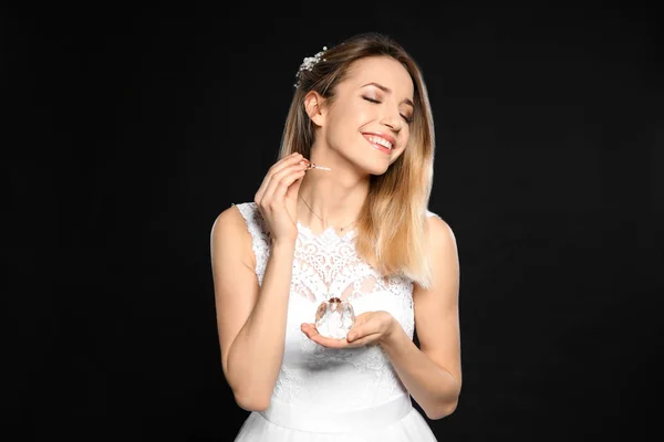 Bela noiva jovem aplicando perfume contra fundo preto — Fotografia de Stock