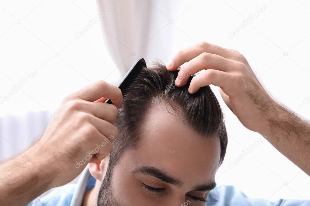 Young man with comb indoors, closeup. Hair loss problem