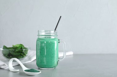 Hafif arka plan karşı masada spirulina tozu ve smoothie mason kavanoz ile Kaşık. Metin için alan