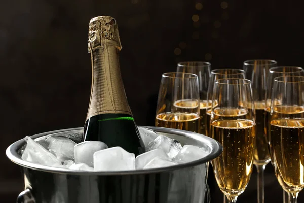 Láhev v kbelíku s ledem v blízkosti sklenic šampaňského na tmavém pozadí — Stock fotografie
