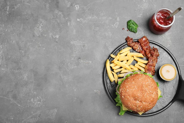 Frigideira com saboroso hambúrguer e batatas fritas em fundo cinza, vista superior. Espaço para texto — Fotografia de Stock