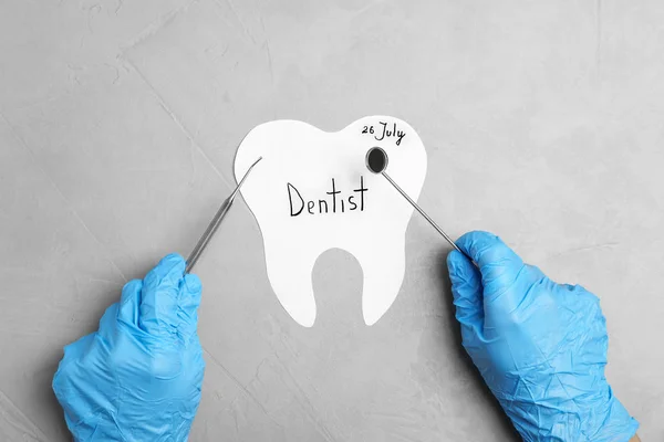 Zahnarzt hält professionelle Werkzeuge über Papierzahn auf grauem Hintergrund, Ansicht von oben — Stockfoto