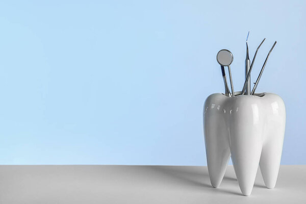 Tooth shaped holder with professional dentist tools on grey background. Space for text
