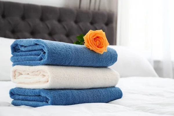 Pilha de toalhas limpas e bela flor de rosa na cama. Espaço para texto — Fotografia de Stock