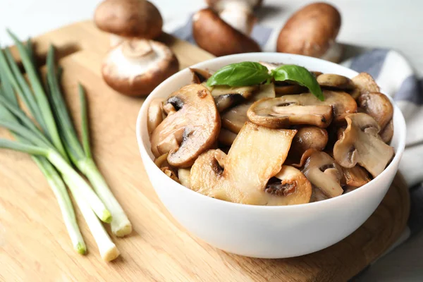Delicious cooked mushrooms with basil in bowl on table