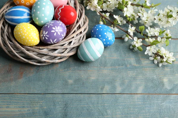 Œufs de Pâques peints dans le nid et branches fleuries sur la table, vue d'en haut. Espace pour le texte — Photo