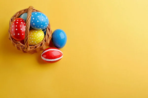 Wicker basket with painted Easter eggs on color background, top view. Space for text — 스톡 사진
