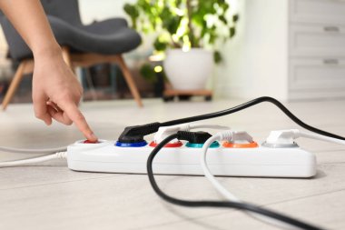 Kadın, evin içinde yerde, uzatma kablosunun düğmesine basıyor, yakın plan. Elektrikçinin profesyonel ekipmanı