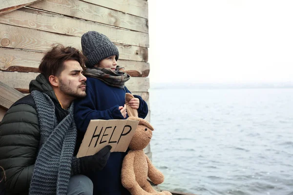 川辺のヘルプサインを持つ貧しい父と子供。テキスト用のスペース — ストック写真