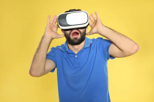 Jovem emocional jogando videogames com fone de ouvido de realidade virtual em fundo de cor — Fotografia de Stock