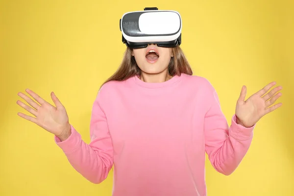Эмоциональная молодая женщина играет в видеоигры с гарнитурой виртуальной реальности на цветном фоне — стоковое фото