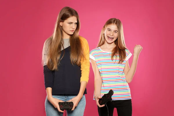 Молодая женщина и девочка-подросток играют в видеоигры с контроллерами на цветном фоне — стоковое фото