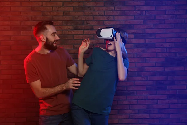 Mulher emocional jogando videogames com fone de ouvido VR e homem feliz perto da parede de tijolo. Espaço para texto — Fotografia de Stock