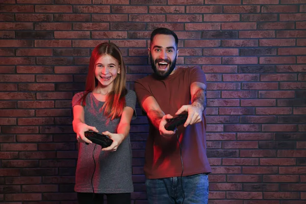 Hombre joven y adolescente jugando videojuegos con controladores cerca de la pared de ladrillo —  Fotos de Stock
