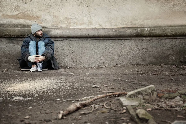 路上で壁の近くに座っている貧しいホームレスの男性。テキスト用のスペース — ストック写真