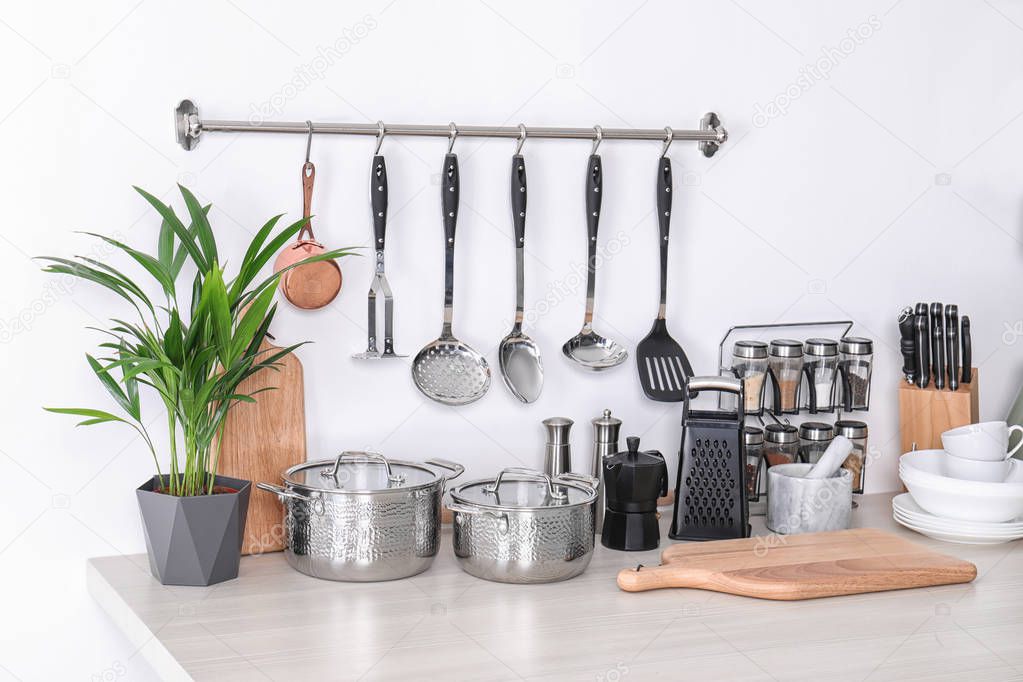 Set of clean cookware, dishes, utensils and appliance on table at white wall