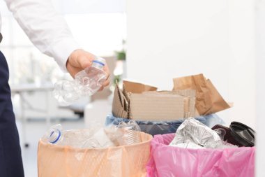 Adam ofiste çöp kutusu içine kullanılmış plastik şişe koyarak, closeup. Atık geri dönüşümü