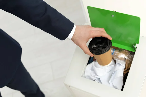 Um homem a pôr xícara de papel usada no caixote do lixo no escritório, perto. Reciclagem de resíduos — Fotografia de Stock