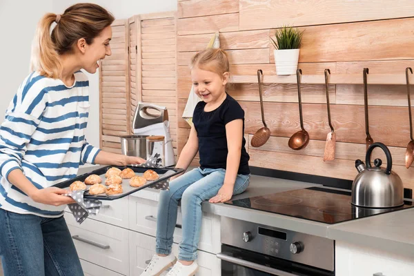 Mujer joven tratando a su hija con galletas horneadas horno casero en la cocina — Foto de Stock