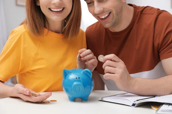 Pareja poniendo monedas en alcancía en la mesa, primer plano. Ahorro de dinero — Foto de Stock