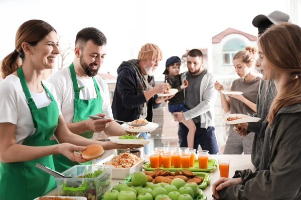 Volunteers giving food to poor people indoors