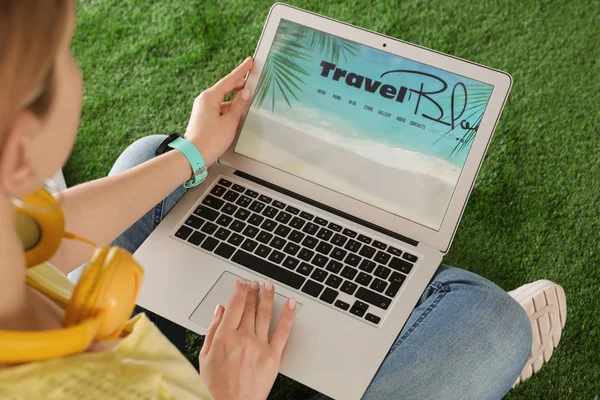 Nő gazdaság laptop nyílt utazási blogger oldalon a mesterséges fű, closeup — Stock Fotó