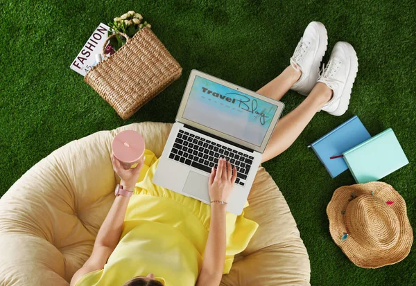 Woman and laptop with travel blogger site on artificial grass, top view — Stock Photo, Image