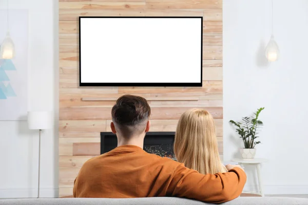 Couple regardant la télévision sur canapé dans le salon avec cheminée décorative — Photo