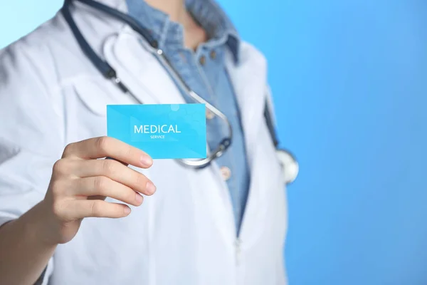 Doctor sosteniendo tarjeta de visita en el fondo de color, primer plano con espacio para el texto. Servicio médico — Foto de Stock