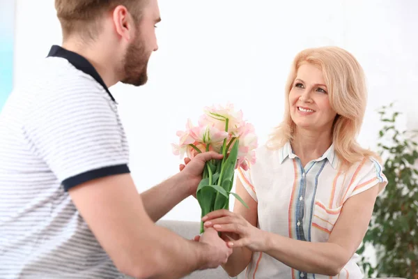 Un giovanotto che si congratula con sua madre matura a casa. Buona festa della mamma — Foto Stock