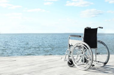 Güneşli bir günde nehir kenarında boş tekerlekli sandalye. Metin için alan