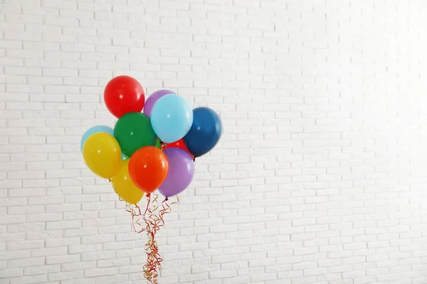 Manojo de globos brillantes cerca de la pared de ladrillo, espacio para el texto. Tiempo de celebración — Foto de Stock