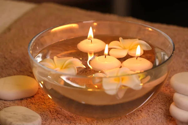 Bowl with water and burning candles on table in spa salon — Stock Photo, Image