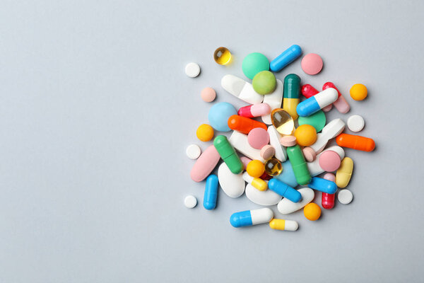 Heap of different pills on grey background, top view. Space for text
