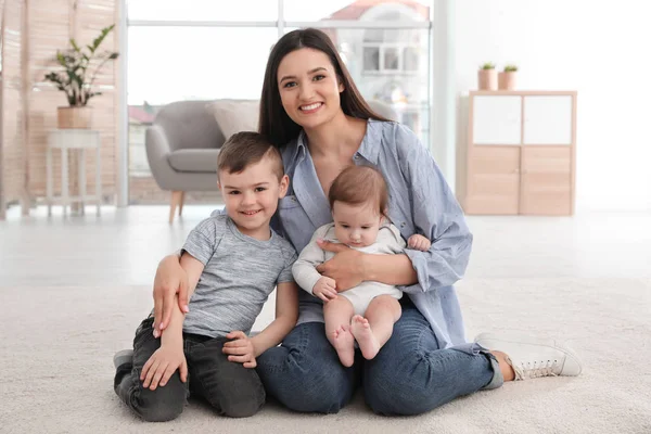 Jonge moeder met haar kinderen zitten samen op de vloer thuis — Stockfoto