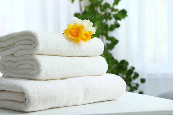 Stack of fresh towels with flowers on table indoors. Space for text — Stock Photo, Image