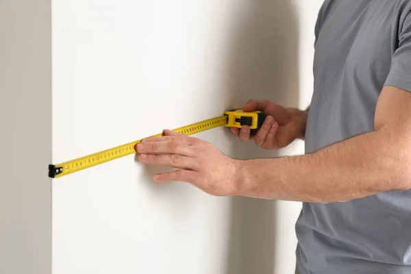 Чоловік вимірює білу стіну в приміщенні, крупним планом. Будівельний інструмент — стокове фото