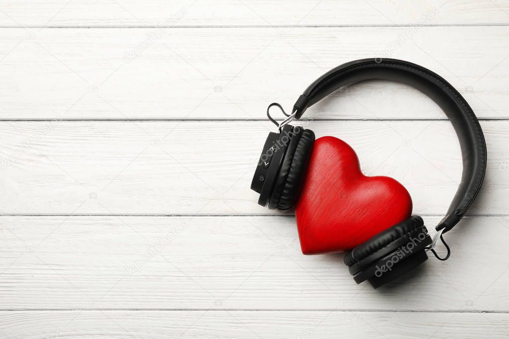 Decorative heart with modern headphones on wooden background, top view. Space for text