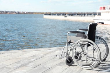 Güneşli bir günde nehir kenarında boş tekerlekli sandalye. Metin için alan