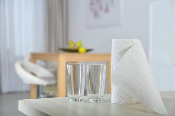 Roll of paper towels and glasses on table indoors. Space for text