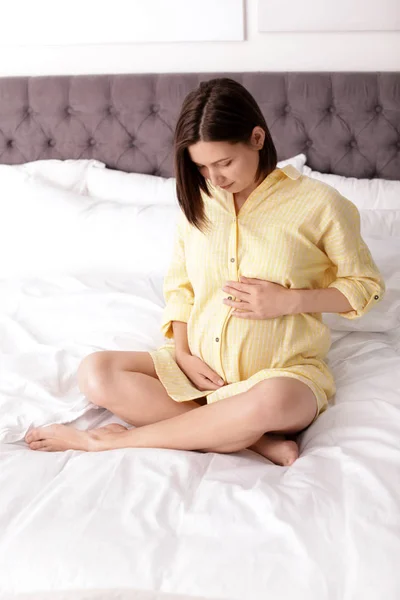 Beautiful pregnant woman sitting on bed at home — Stock Photo, Image