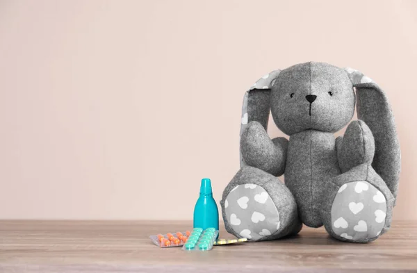 Coelho de brinquedo e medicamentos na mesa contra fundo de cor, espaço para texto. Hospital infantil — Fotografia de Stock