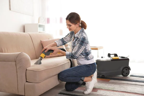 Woman removing dirt from sofa with vacuum cleaner at home