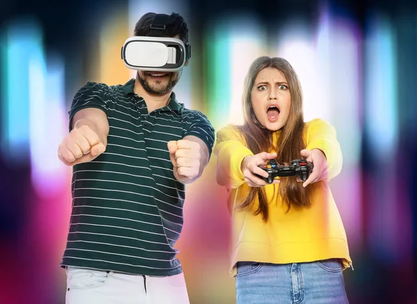 Homem vestindo fone de ouvido VR e mulher com controlador jogando jogos de vídeo em fundo colorido — Fotografia de Stock