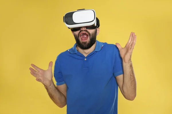 Emotional young man playing video games with virtual reality headset on color background — Stock Photo, Image