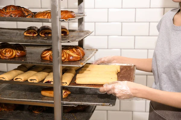 Baker taking out tray with pastry from rack in workshop, closeup